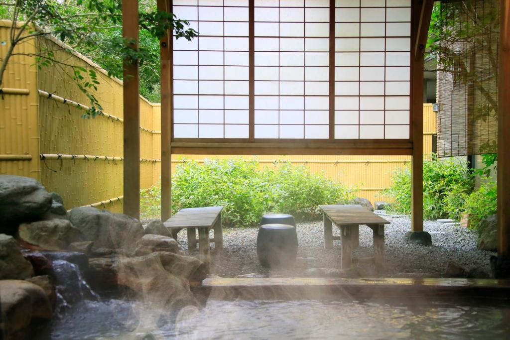 Rock-lined outdoor hot spring bath at EN RESORT Re’Cove Hakone beside a bamboo screen and garden